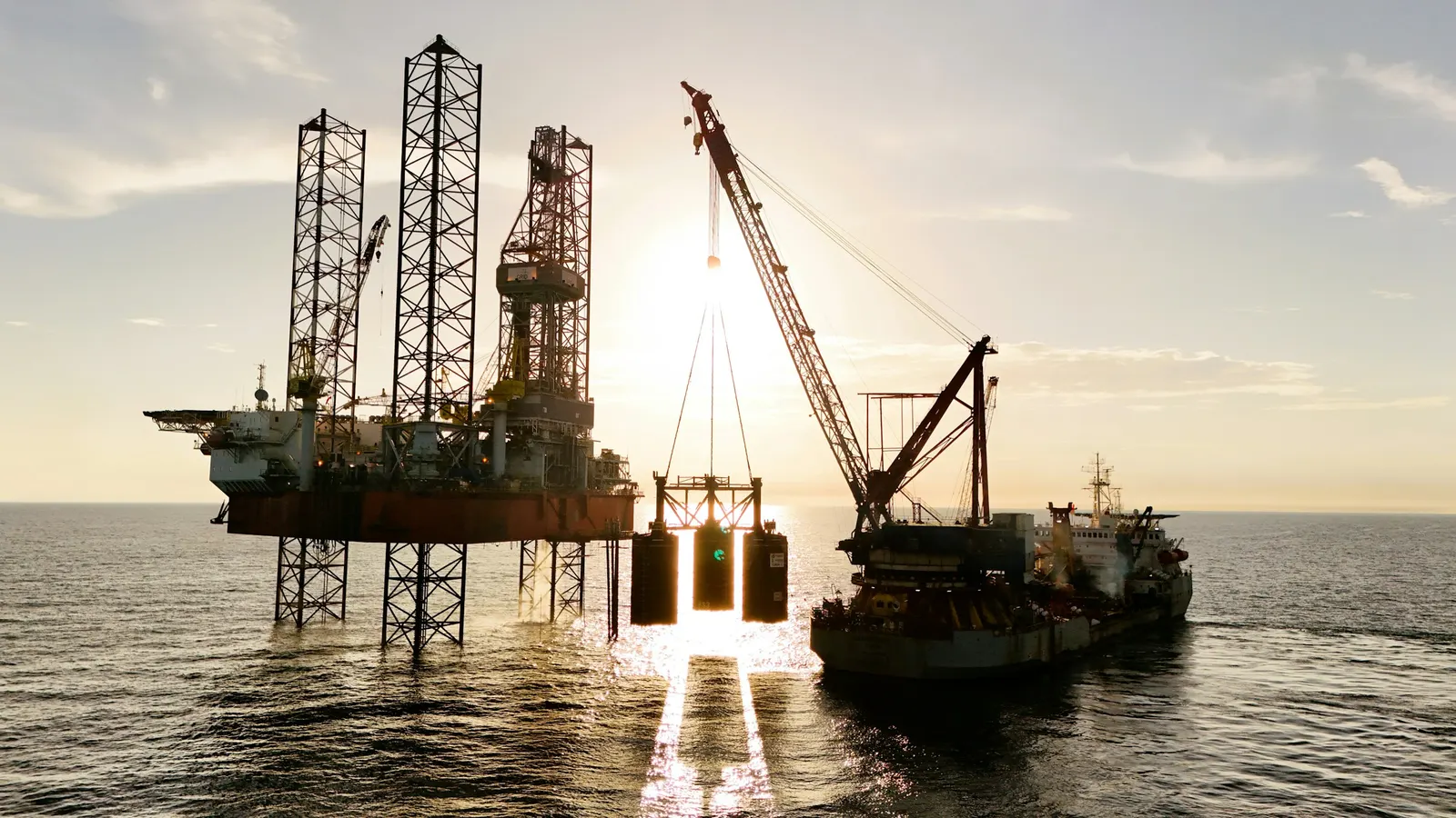 Offshore rig being serviced by a supply vessel at sunset