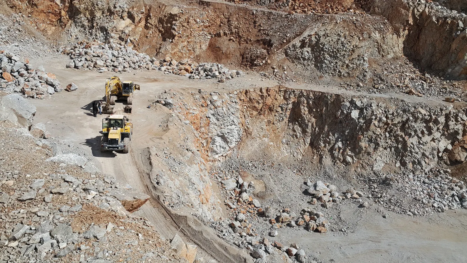 Excavator and wheel loader working on a haul road in an open-pit quarry